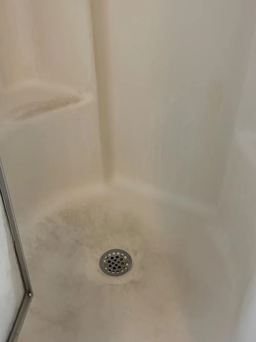 Shower pan and drain before cleaning in Clinton, MA, with mildew staining around the drain