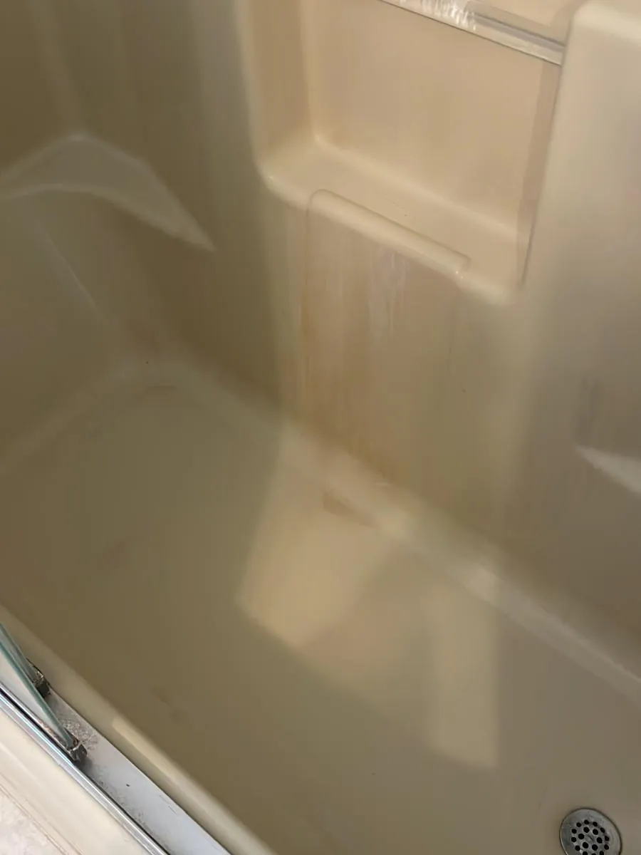 Shower surround wall before cleaning in Clinton, MA, with brown rust and mineral streaks running down the panel